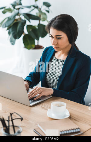 Junge Geschäftsfrau Tippen auf Laptop von Tabelle im Büro Stockfoto