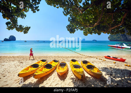 Frau im rosa Kleid zu Fuß auf der Phranang Beach mit gelben Kajak Boot in Thailand Stockfoto