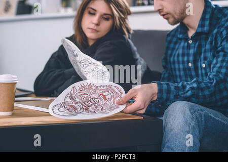 Verschiedene Tattoo Designs in den Händen des jungen Paares im Tattoo Salon Stockfoto