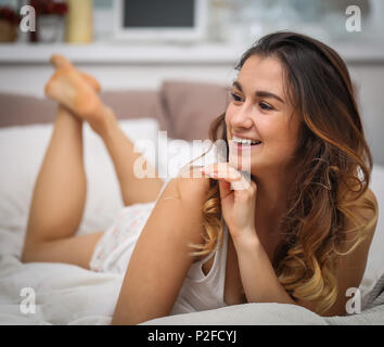 Schöne junge Mädchen mit langen Haaren liegen auf einem weißen Bett, Foto closeup Stockfoto