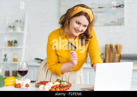 Lächelnd schöne Frau mit Kreditkarte und Laptop in der Küche Stockfoto