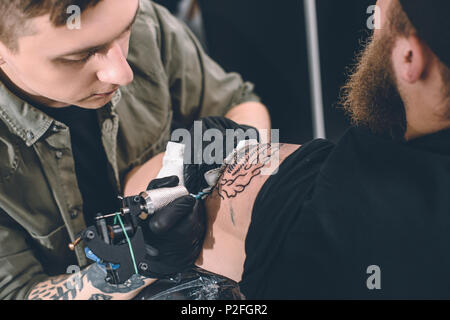 Tattoo Artist und bärtiger Mann während des Tätowierens Prozess im Studio Stockfoto