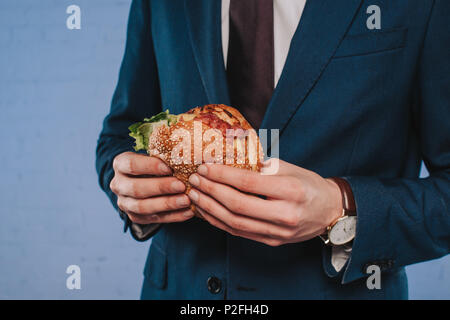 7/8 Schuß von Geschäftsmann in Anzug holding Burger Stockfoto