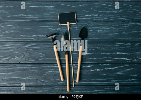 Flach mit angeordnet, Gartengeräte und leere Schiefertafel auf hölzernen Tischplatte Stockfoto