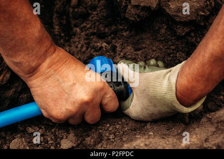 Der Arbeitnehmer verdreht die gemeinsame in den Schlauch im Garten im Garten Stockfoto