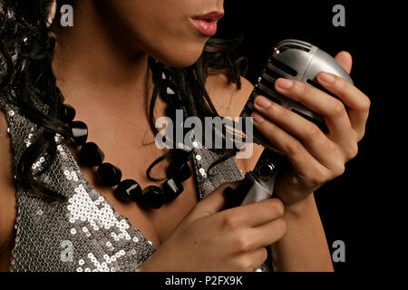 Young woman holding and singing into a retro-stlye microphone Stockfoto