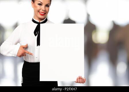 Schöne Geschäftsfrau und lächelnd ein weißes Schild mit Kopie Platz für Werbung und Text auf einem unscharfen Hintergrund des Amtes. Stockfoto