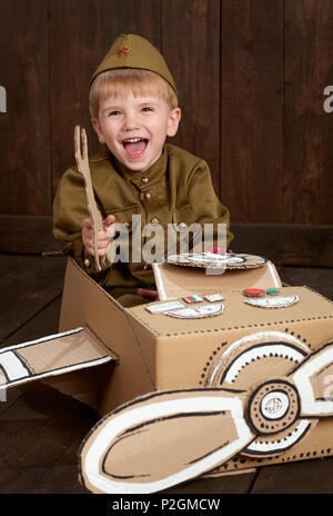 Kinder Jungen sind als Soldat in retro militärische Uniformen Reparatur ein Flugzeug von Karton, dunklen Hintergrund, retro style Stockfoto