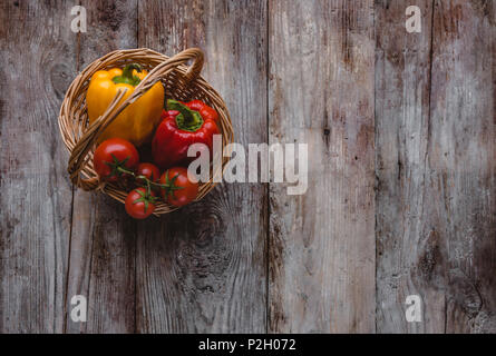 Blick von oben auf die Paprika und Tomaten in Weidenkorb auf hölzernen Tisch Stockfoto