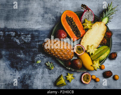 Blick von oben auf die Ananas, Rambutan, pitaya, Passionsfrüchte, Kumquats, Papayas, Karambolen und Mango in der Platte auf dem Tisch Stockfoto