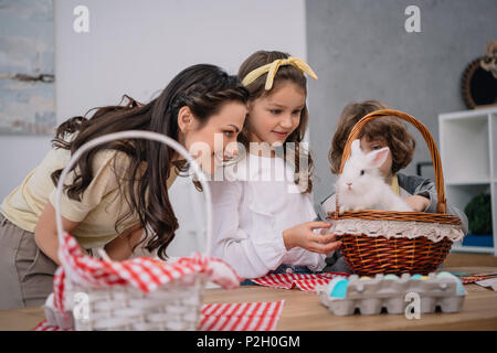 Kinder und Mutter spielt mit Ostern Kaninchen zu Hause auf dem Tisch Stockfoto