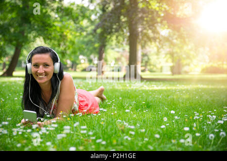 Junge Frau liegt auf der Wiese und das Hören von Musik Stockfoto