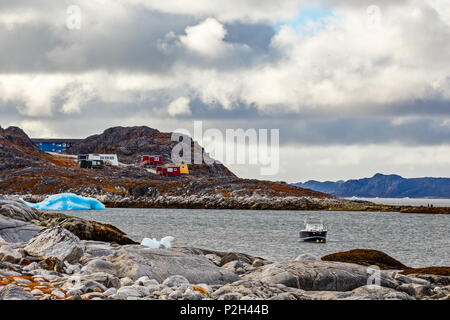 Arktische Küste Stein, Motorboot und blau Iceberg schwimmend in der Bucht mit kleinen bunten Häusern auf den Felsen im Hintergrund, Nuuk, Grönland Stockfoto