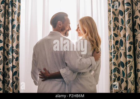 Ansicht der Rückseite des Paar mittleren Alters in der Liebe tragen Bademäntel und lächeln einander im Hotel Zimmer Stockfoto