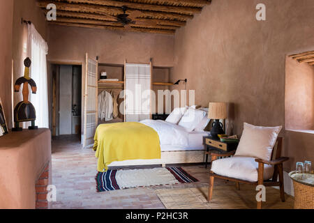 Rattan Bett und Charlotte Perriand Lampe im Schlafzimmer mit Erde Mauern, Terrakotta-Boden und traditionellen Berber Holzdecke. Die wolle Bettdecke kommt aus Stockfoto