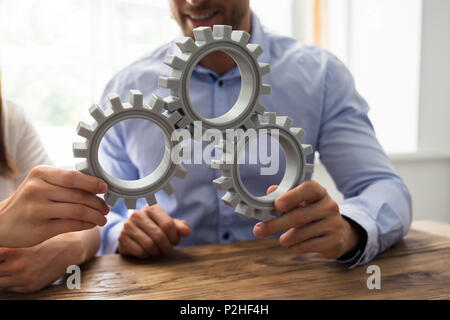 In der Nähe von zwei Geschäftsleute verbinden Zahnräder über Holz- Schreibtisch im Büro Stockfoto