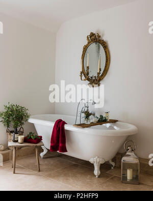 Antike vergoldete Spiegel im Badezimmer mit freistehender Badewanne, Kalkstein Boden und kleinen hölzernen melken Hocker. Stockfoto