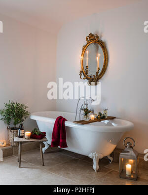 Antike vergoldete Spiegel im Badezimmer mit freistehender Badewanne, Kalkstein Boden und kleinen hölzernen melken Hocker. Stockfoto