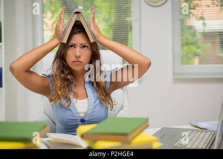 Schöne junge Frau langweilig beim Lernen in der Bibliothek. Sie hält Buch über ihrem Kopf. Stockfoto