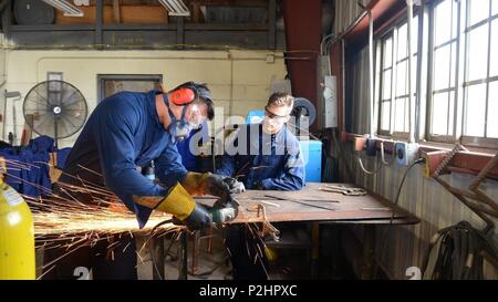 U.S. Coast Guard Petty Officer 1st Class Brett Malone, ein Schaden controlman mit der Boje Ausschreibung USCGC Sequoia (WLB-215), beobachtet Petty Officer 3. Klasse Peter Ritchel, auch ein DC, wie er Metall schleift Klimaanlage Halterungen an den USA Civic's Action Team Camp Katuu in Palau, Sept. 14, 2016 herzustellen. Coast Guard Mitglieder die Katze mit Service und Wartung der Anlagen unterstützt. (U.S. Coast Guard Foto von Chief Petty Officer Sara Mooers) Stockfoto