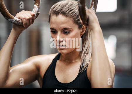 Passen junge Frau in Sportswear konzentriert sich vor Arbeiten an Ringe an der Turnhalle Stockfoto