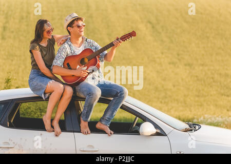 Junge hipster Paar mit akustischer Gitarre sitzt auf dem Dach in der Natur. Liebe und Reisen Konzepte. Stockfoto