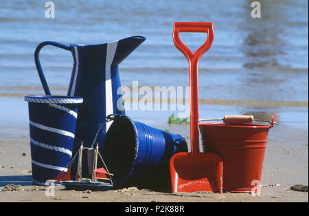 Nahaufnahme von roten Schaufel und Spaten am Strand mit blauer Emaille Kanne und Eimer Stockfoto