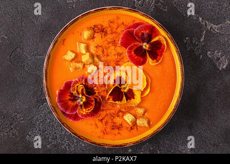 Kürbis/Karotten Suppe mit Safran und essbaren Blüten Stiefmütterchen, Ansicht von oben. Stockfoto