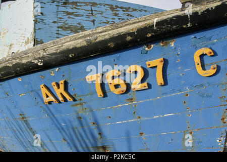 Alte verwitterte Holz Fischerboot mit gelben Registrierung Buchstaben und Zahlen auf Peeling blaue Farbe auf dem Rumpf Stockfoto