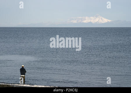 Lone Fischer, die in den seichten Brandung an der Küste, am Rande eines ruhigen Ozean auf einem langweiligen, grauen Tag Stockfoto