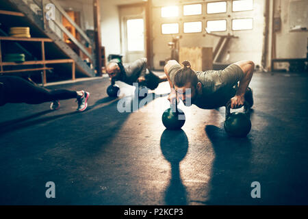 Passen junge Mann tun pushups auf kurzhanteln während der Arbeit aus während einer Übung Klasse in einer Turnhalle Stockfoto