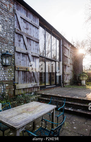 Gartenmöbel auf der Terrasse der Scheune convesrion mit großen Fenstern und Fensterläden aus Holz, Sussex Stockfoto