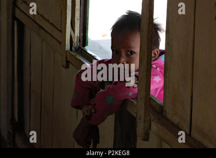 Eine wehmütige Kind durch ein offenes Fenster in ein Klassenzimmer, Blickkontakt mit der Kamera. Stockfoto