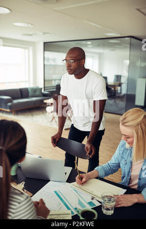 Afrikanische Unternehmer im Gespräch mit Kollegen um einen Tisch während einer Konferenz sitzen zusammen in einem modernen Büro konzentriert Stockfoto