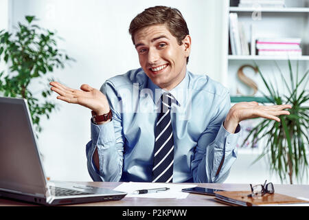 Weiß nicht, was ich tun soll. Büroangestellter breitete seine Hände. Foto junger Mann bei der Arbeit im Büro. Business Konzept Stockfoto