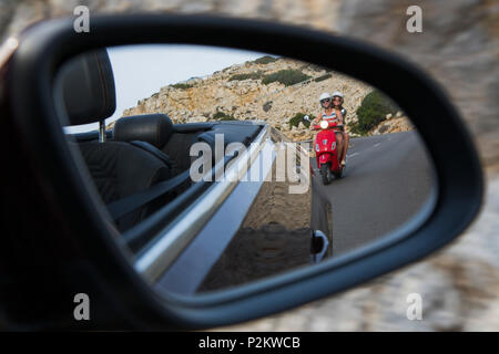 Rückspiegel Blick auf junge Paar Reiten eine rote Vespa Roller auf der Straße entlang Cap de Formentor Halbinsel mit Faro de Formentor Stockfoto