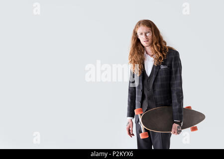 Stilvolle Geschäftsmann mit Ingwer Haar holding Longboard und Kamera isoliert auf weißem Stockfoto