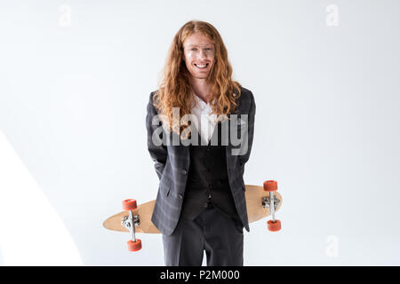Lächelnd stilvolle Geschäftsmann mit lockigem Haar holding Longboard oben zurück Stockfoto