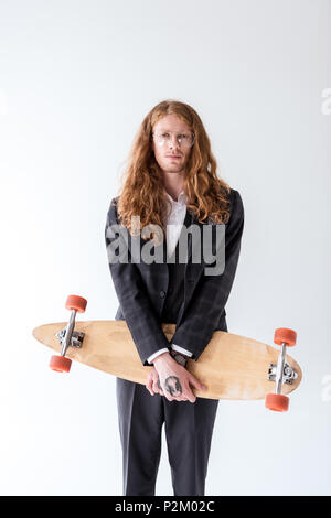 Stilvolle Geschäftsmann mit lockigem Haar holding Longboard isoliert auf weißem Stockfoto