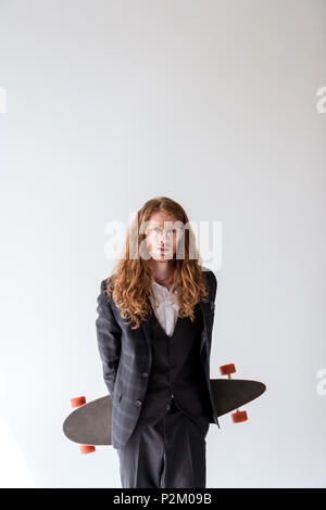 Stilvolle Geschäftsmann mit lockigem Haar holding Longboard isoliert auf weißem Stockfoto