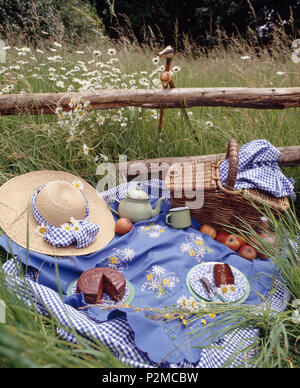 Still-Life von Stroh Hut und Weidenkorb auf blauem Tuch für die Tea time Picknick mit Schokoladenkuchen eingestellt Stockfoto