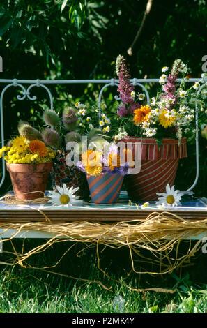 In der Nähe von orange Tagetes und Sommerblumen in Stoff Blumentöpfe auf schmiedeeisernen Garten Bank Stockfoto