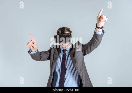 Junge Unternehmer im VR-Headset nach oben isoliert auf Grau Stockfoto