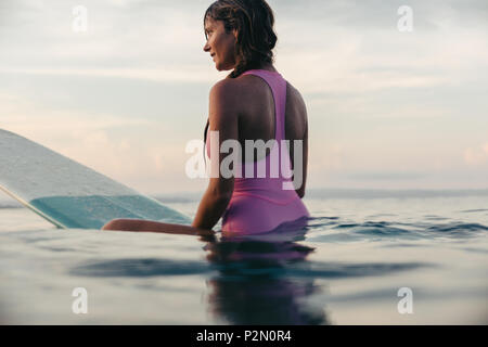 Schöne Frau sitzt auf Surfbrett im Meer bei Sonnenuntergang Stockfoto