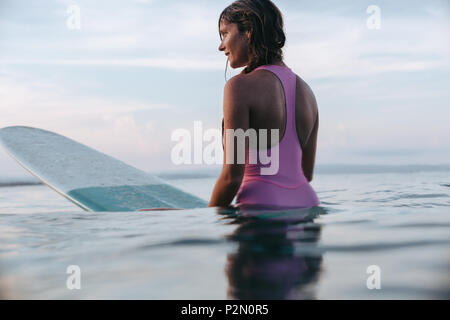 Attraktive Frau sitzt auf Surfbrett im Meer bei Sonnenuntergang Stockfoto