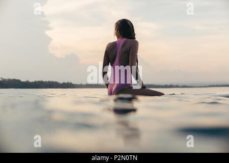 Silhouette der Surfer in rosa Badeanzug sitzen auf Surfboard bei Sonnenuntergang Stockfoto