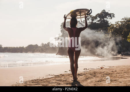 Rückansicht der Sportlerin, die Surfen am Kopf beim Gehen auf die Küste Stockfoto