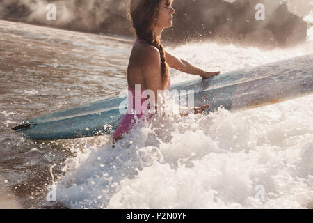 Junge Frau, die das Surfen in die Hände beim Gehen in Ocean Stockfoto