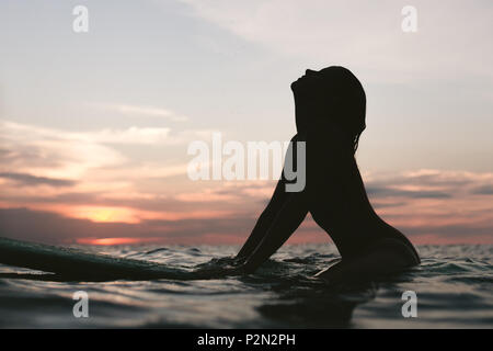 Silhouette einer Frau ruht auf Surfen im Ozean auf Sonnenuntergang Stockfoto