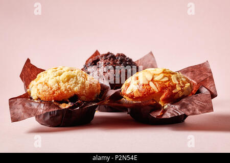 Mandel, Heidelbeere und Schokolade Muffins in braunem Papier auf rosa Hintergrund Stockfoto